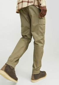 Cargo broeken in olijfgroen stof met elastische manchetten, featuring zijzakken en een losse pasvorm. Gecombineerd met bruine wandelschoenen.