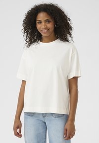 T-shirt en coton blanc avec une coupe décontractée, des manches courtes et un col rond, associé à un jean en denim clair. Texture lisse, design minimal.