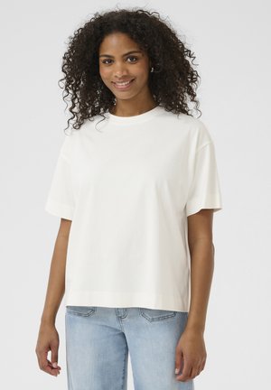 Vit bomullströja med avslappnad passform, korta ärmar och rund halsringning, kombinerad med ljusa denimjeans. Slät textur, minimalistisk design.