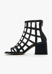 Black open-toe ankle boots with a grid design, featuring a chunky heel and a side zipper. Made of textured synthetic material.