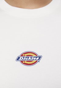 Hvit bomulls t-skjorte med en fargerik rektangulær logo med "Dickies" i fete blå bokstaver, satt mot en rød og gul bakgrunn.