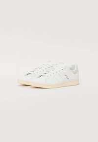 Hvide lædersneakers med lavtopdesign, beige accenter, perforerede detaljer på siderne og en cremet gummisål.