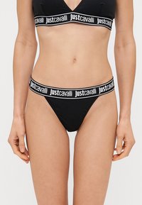 Čierny bikinový set s trojuholníkovým braletom a tangami. Obe majú kontrastný biely branding na elastických pásoch. Hladká textúra látky.
