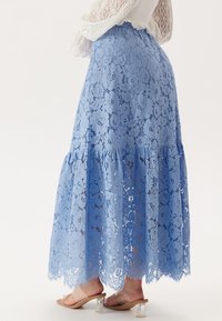 Ljusblå spetsmaxikjol med blommönster, lagerdesign, vågig fåll och genomskinlig textur. Kombinerad med transparenta blockklacksandaler.