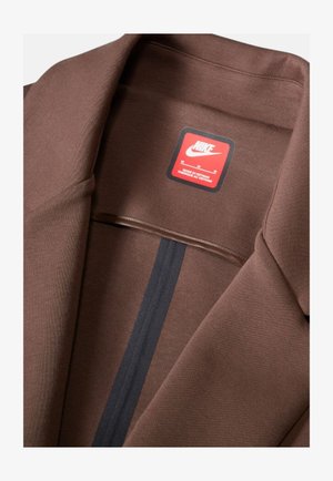 Collare di un capo Nike marrone con etichetta rossa e bianca del marchio con il testo "Made in Vietnam" e una striscia nera verticale all'interno del tessuto.