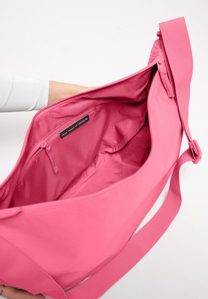 Hand hält eine große pinke Schultertasche offen mit einem innenliegenden Reißverschlussfach mit der Aufschrift "VOM MÜLL ZUM SCHATZ."