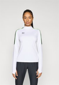 White long-sleeve shirt with high collar, green accents on the shoulders, and black logo. Worn with dark gray pants. Smooth texture.