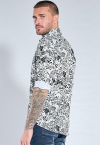 Hemd zum Zumknöpfen mit einem schwarz-weißen Blumenmuster, kurzen Ärmeln mit weißem Bündchen und geradem Schnitt. Strukturierter Stoff.