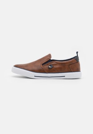 Basket slip-on en cuir marron avec semelle en caoutchouc blanche et détail de bordure noire, vue de côté sur un fond uni.
