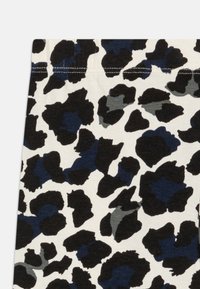Tissu imprimé léopard sur fond crème avec des taches noires, navy et grises ; présente une texture douce et une taille élastique.