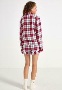 Ensemble de pyjama court en vichy rouge et blanc avec une chemise à boutons et un short dotés de bords festonnés. Tissu en coton et coupe décontractée.