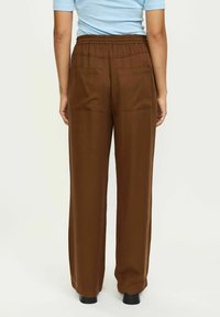 Bruine, wijde broek gemaakt van een soepele stof. Beschikt over een elastische tailleband en twee achterzakken; de pijpen zijn van volledige lengte.