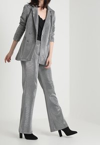 Costume métallique argenté avec un blazer croisé et un pantalon droit. Porté avec un haut noir et des bottines à talons noires.