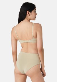 Set di lingerie beige con reggiseno a chiusura posteriore e spalline regolabili, abbinato a pantaloni alti, realizzato in materiale morbido ed elastico.