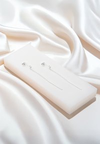 Silverhängande örhängen med en polerad yta, som har en kedjedesign och avlånga stavaccent, visade på en vit rektangulär låda.