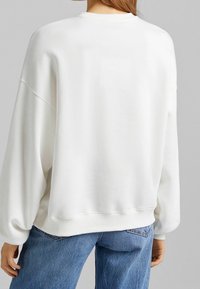 Sweat-shirt blanc surdimensionné en coton doux, avec un col rond, des épaules tombantes et des poignets côtelés. Associé à un jean en denim bleu.