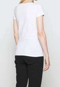 Hvid kortærmet tætsiddende T-shirt med rund halsudskæring, glat bomuldsstof og en ren finish ved kanten og ærmerne, parret med sorte bukser.