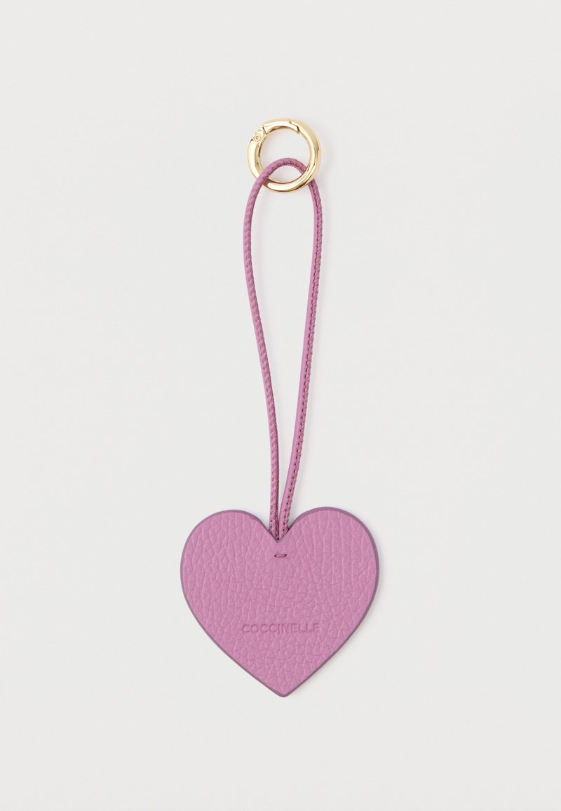 Breloc în formă de inimă, din piele mov, cu o suprafață texturată și un șnur asortat. Dispune de un inel de prindere de culoare aurie.