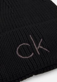 Cappello in maglia nera con texture a costine e un sottile logo ricamato "ck" in grigio sulla parte frontale.