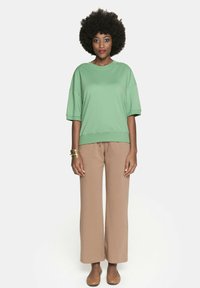 Zielona, oversize'owa koszulka z krótkim rękawem, zestawiona z luźnymi, beżowymi spodniami o szerokich nogawkach. Gładki materiał, swobodny krój i subtelny kontrast kolorów.