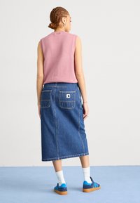Pulover roz fără mâneci, fustă midi din denim cu buzunare la spate, adidași albastre și șosete albe. Textură moale, design casual și culori contrastante.