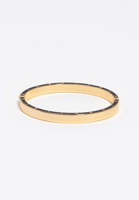 Pulsera de brazalete de oro con un anillo superior de esmalte negro que presenta letras doradas espaciadas uniformemente alrededor del borde sobre un fondo blanco.