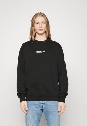 Sort bomulds sweatshirth med rund halsudskæring og hvid "REPLAY" grafik på brystet samt ribbet manchetter. Båret sammen med lyseblå denimjeans.