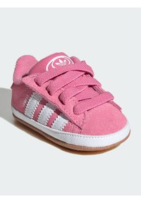 Růžové semišové tenisky s bílými pruhy, kulatou špičkou, texturovanými tkaničkami a bílou gumovou podrážkou. Obsahují logo na jazyku.