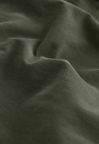 Dark green fabric with soft folds and fine woven texture, creating gentle shadows and highlights across the surface.