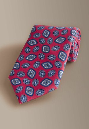 Rode zijden stropdas met een herhalend blauw-wit paisleypatroon, opgerold met een gladde textuur. Accenten zijn onder meer gekartelde randen.