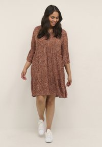 Braunblümiges Kleid mit Dreiviertelärmeln, ausgestelltem Rock und geraffter Taille. Kombiniert mit weißen Sneakern. Weicher Stoff, lässiges Design.