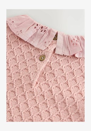 Top tricoté rose clair avec un motif en diamant texturé, un col volanté et deux boutons marron le long de l'encolure.