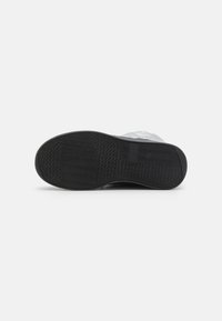 Black rubber sole with a textured pattern. Upper part features a smooth, light silver material. Rounded shape designed for comfort.