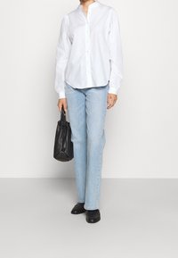 Chemise blanche à manches longues avec boutons, jean droit bleu clair, sac à main noir texturé et mocassins noirs. Design minimaliste, couleurs classiques.