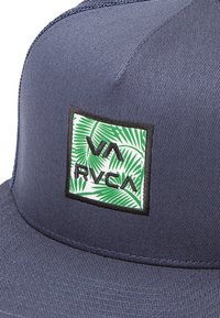 Navy cap with a curved visor; features a square patch with green palm leaf design and black embroidered "RVCA" logo on the front.
