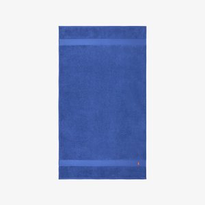 Toalla azul hecha de algodón suave con una superficie texturizada. Presenta dos franjas horizontales y un pequeño logo en la esquina inferior.