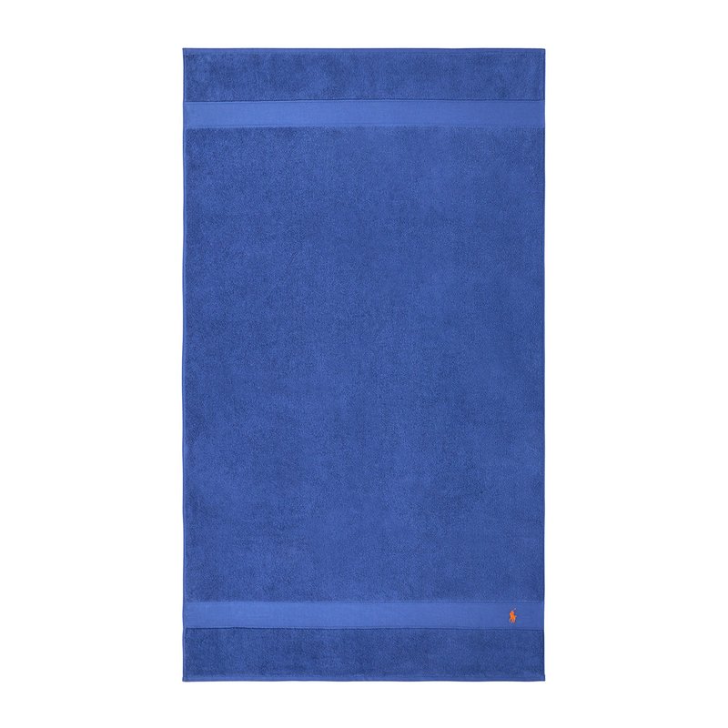 Μπλε πετσέτα από απαλό βαμβάκι με υφή στην επιφά νεια. Διαθέτει δύο οριζόντιες ρίγες και ένα μικρό λογότυπο στην κάτω γωνία.
