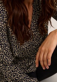 Blouse marine à motif floral crème, avec un design à col en V et des manches longues. Le tissu semble doux avec un léger éclat.