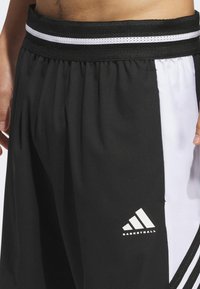 Black basketball shorts made of lightweight fabric with a white side panel, elastic waistband, and Adidas logo on the left leg.
