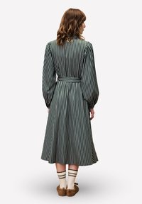 Robe à manches longues rayée verte avec une taille cintrée, une jupe évasée et des rayures verticales. Portée avec des chaussettes rayées à mi-mollet et des pantoufles douces.