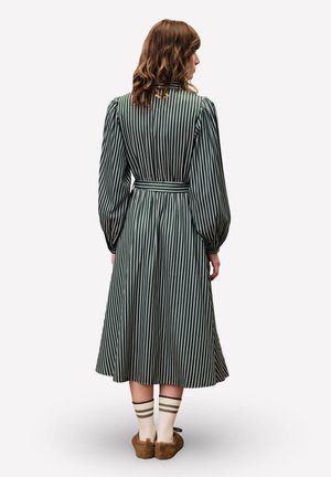 Groen gestreepte lange mouw jurk met een strakke taille, uitlopende rok en verticale strepen. Draag het met kniekousen met strepen en zachte slippers.