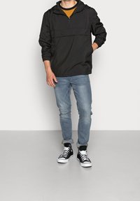 Svart huvtröja med halvlång dragkedja, har en känguruficka och justerbar huva, kombinerad med ljusblå jeans och svarta hög-top sneakers.