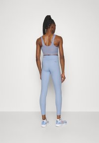 Světle modrý sportovní crop top a odpovídající legíny, s hladkou texturou a přiléhavým střihem, doplněné světle modrými sportovními botami.