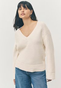 Maglione color crema con scollo a V, texture a coste, maniche lunghe e vestibilità rilassata, abbinato a jeans blu.