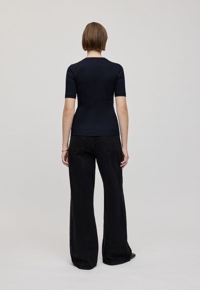 Top negru cu mânecă scurtă, ajustat, cu decolteu rotund, asortat cu pantaloni negri, cu talie înaltă și croială largă. Material neted, cu textură minimă.