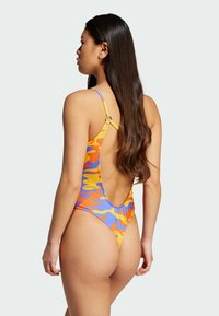 Μαγιό με σχέδιο χαμηλής πλάτης, διακοσμημένο με πολύχρωμο αφηρημένο μοτίβο σε πορτοκαλί, μπλε και κίτρινο. Λεπτές τιράντες και απαλό υφασματικό υλικό.
