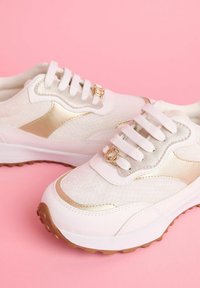 Weiße Sneakers mit metallisch goldenen Akzenten, strukturiertem Mesh-Obermaterial, runden Schnürsenkeln und Gummisohle mit kleinen Traktionspunkten.