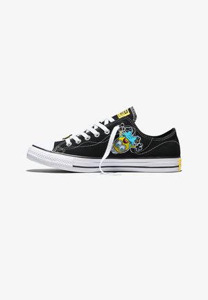 Black low-top sneaker with white sole and laces, featuring a joyful cartoon minion character on the side and yellow branding accents.