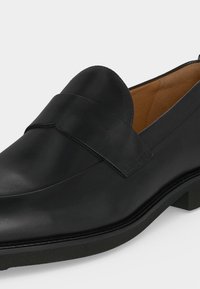 Chaussure habillée en cuir noir sans lacets avec petit talon et finition lisse, dotée d'une large bride sur le dessus et d'une doublure intérieure couleur tabac.