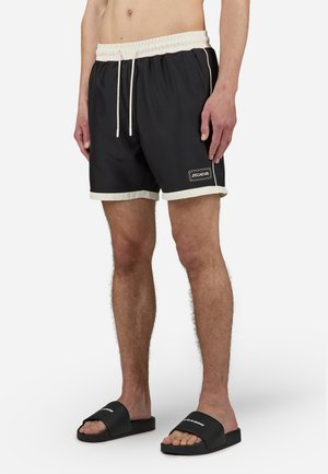 Sorte badebukser med en kontrastfarge i krem på midjen og kanten, med en brodert logo på forsiden. Glatt tekstur, avslappet passform.